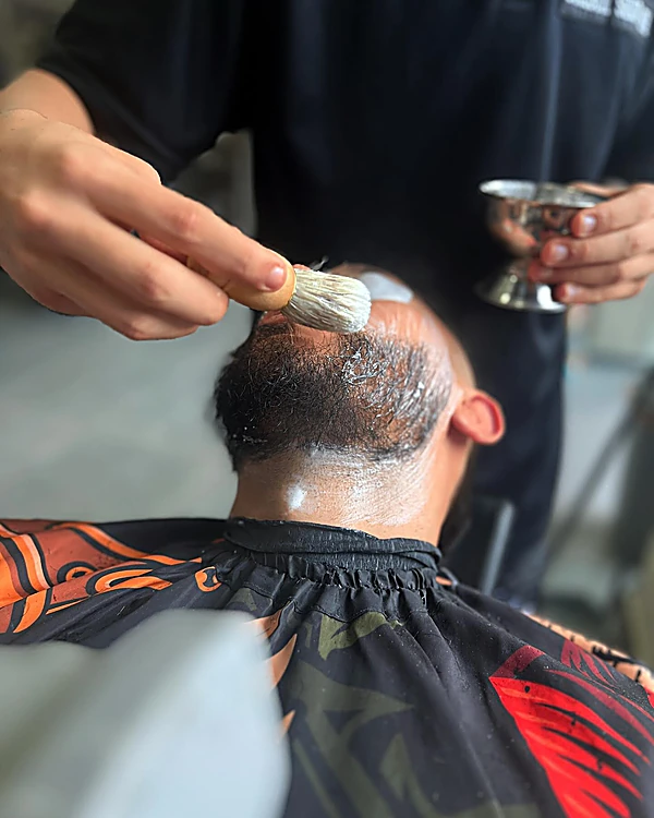 Barbero aplicando espuma con brocha en la barba y el cuello