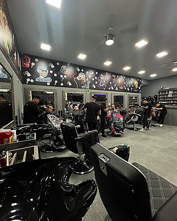El salón trabajando: barberos atendiendo en varias estaciones bajo el mural